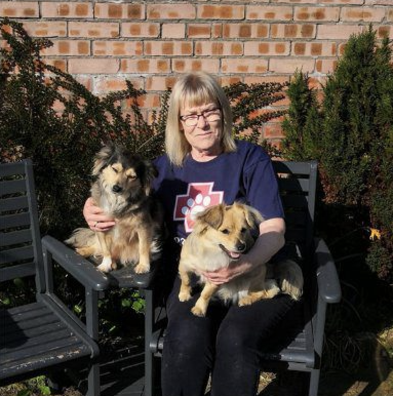 A photo of Paws2Rescue team member Maureen sitting outside holding two small dogs